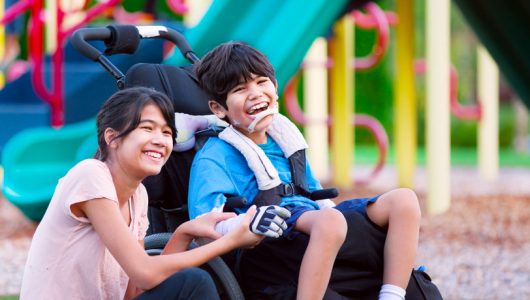 34156613 - sister sitting next to disabled brother in wheelchair at playground
